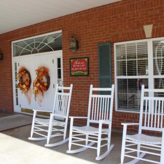 A cozy front porch adorned with white rocking chairs and festive wreaths on the entrance doors of a brick building.