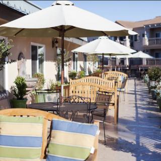 An inviting outdoor patio with wooden benches, tables, and umbrellas for shade.