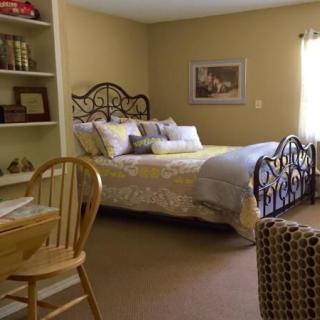 A cozy bedroom with a well-decorated bed, bookshelves, and a wooden chair by the window.