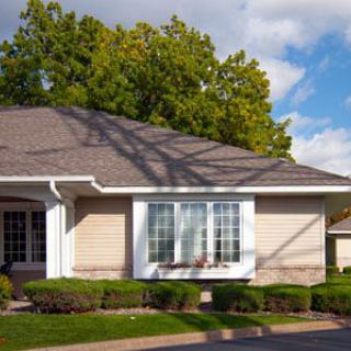 A suburban house with a neatly trimmed front yard and lush trees in the background.