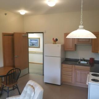 A cozy apartment kitchen with wooden cabinets, a dining table, and a white refrigerator.