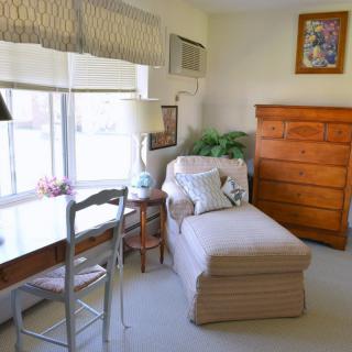 A cozy living room with a chaise lounge, wooden dresser, and a desk by the window.