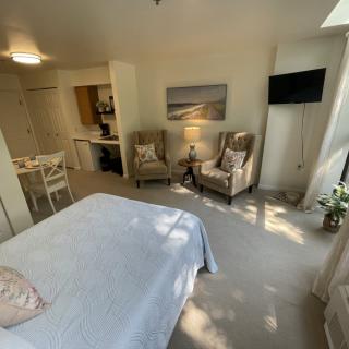 A cozy bedroom with a bed, two chairs, and a wall-mounted TV.