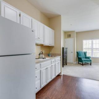 A cozy kitchen and living area with white cabinets, a refrigerator, hardwood floor, and a comfortable chair by the window.