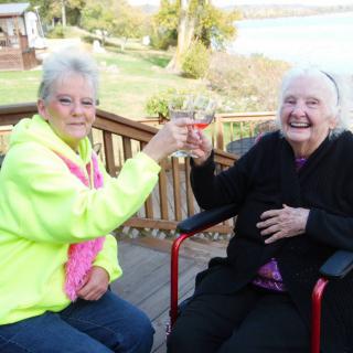 Two elderly women enjoying a cheerful toast on a balcony.