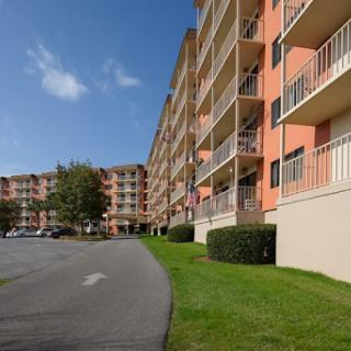 A view of a multi-story apartment building with balconies, surrounded by well-maintained landscaping under a clear blue sky.