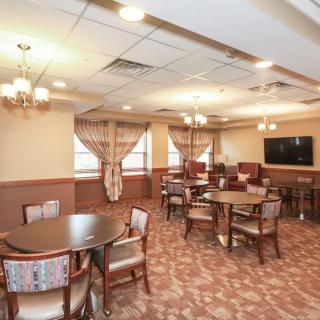 A cozy dining room with multiple tables and chairs, elegantly decorated with chandeliers and curtains, featuring a television on the wall.