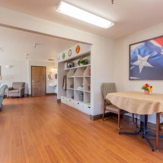 A well-lit room with a table, chairs, and shelves, featuring artwork on the wall.