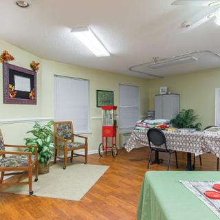 A cozy room with tables, chairs, and a popcorn machine, decorated with plants and artwork.