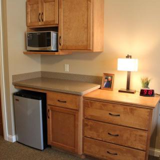 A compact kitchenette setup with a microwave, mini fridge, and wooden cabinets.