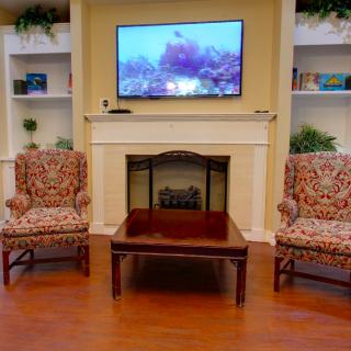 A cozy living room with a television above the fireplace, flanked by bookshelves and armchairs.