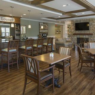 A cozy restaurant interior featuring a bar and dining area with wooden furniture and a brick accent wall.