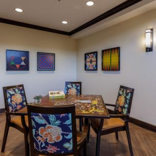A cozy dining area with a beautifully set table surrounded by floral-patterned chairs, adorned with vibrant artwork on the walls.