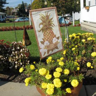 A garden with a decorative pineapple sign surrounded by vibrant yellow flowers.