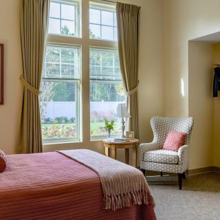 A cozy bedroom with a large window, armchair, and neatly made bed.