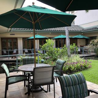 Outdoor patio area with tables, chairs, and green umbrellas surrounded by lush garden.