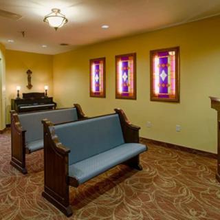 A small chapel featuring wooden pews, stained glass windows, and a piano in a warmly lit interior.