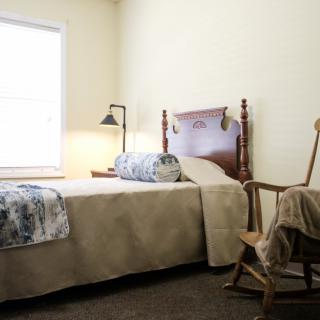 A cozy bedroom with a single bed, rocking chair, and lamp by the window.