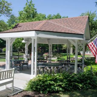 A quaint gazebo in a park setting with benches and an American flag, surrounded by greenery.