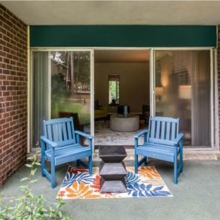 A cozy patio with blue chairs and a colorful rug, leading into a living room through sliding glass doors.