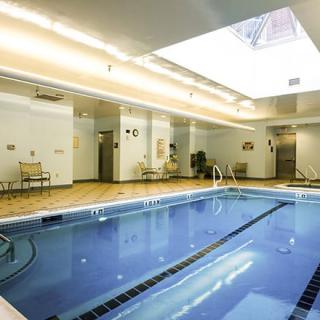 A well-lit indoor swimming pool with a skylight, surrounded by chairs and modern decor.