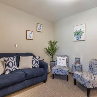 A cozy living room with a navy sofa, patterned chairs, and decorative artwork on the walls.