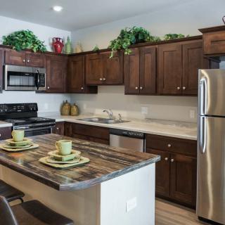 A modern kitchen with wooden cabinets, stainless steel appliances, and an island countertop decorated with plants.