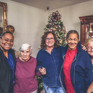 A group of people smiling in front of a decorated Christmas tree indoors.