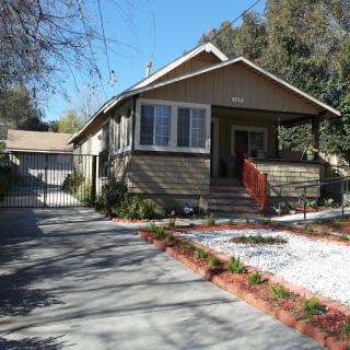 A charming single-story house with a driveway and landscaped front yard surrounded by trees.