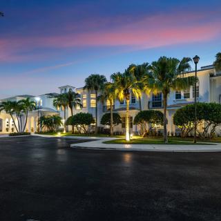 A modern building with palm trees at dusk, illuminated by outdoor lighting.