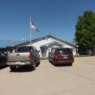 A small building with cars parked in front, under a clear blue sky with a flagpole.