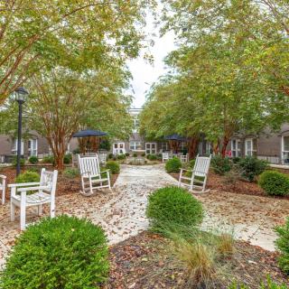 A tranquil garden area with white rocking chairs and a pathway lined by trees.