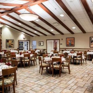 An empty restaurant dining area with neatly arranged tables and chairs, featuring wooden ceiling beams and soft lighting.