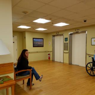 A woman sitting in a hospital waiting area next to a wheelchair.