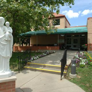 A serene entrance to a building, featuring a statue and well-maintained landscaping.