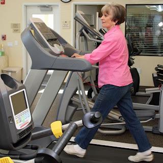 An elderly woman exercises on a treadmill in a gym.