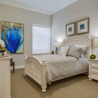 A well-decorated bedroom featuring a bed with neutral bedding, artwork, and stylish lamps.