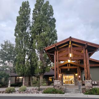 A welcoming entrance to a beautifully designed building surrounded by lush trees under a cloudy sky.
