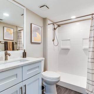 A modern and minimalist bathroom with a shower, sink, and toilet.
