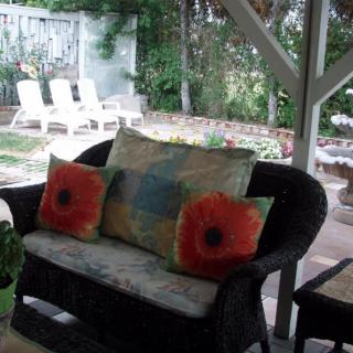 A cozy outdoor patio area with a sofa and vibrant cushions, overlooking a garden.
