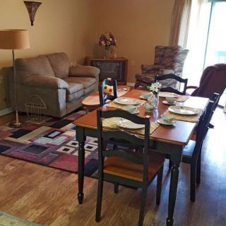 A cozy dining area with a table set for a meal, adjacent to a comfortable living space with sofas and a lamp.