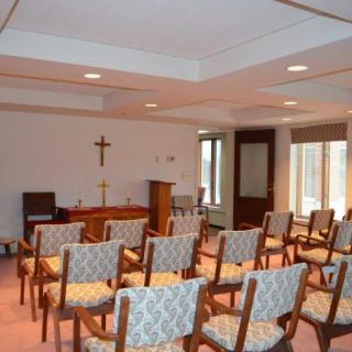 An empty chapel with rows of chairs and a cross on the wall.