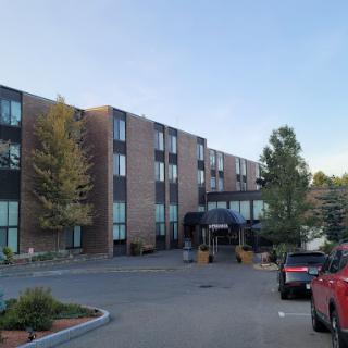 A modern hotel building with a parking lot and surrounding trees during daytime.