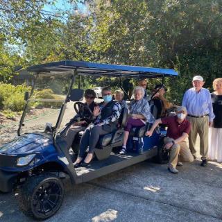 A group of people enjoying a sunny day, gathered around and on a golf cart.