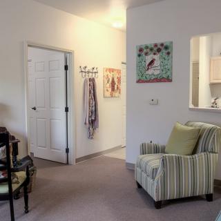 A cozy living room with a striped armchair, artwork on the walls, and a view into an adjacent kitchen area.