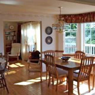 A sunlit dining room featuring wooden furniture and large windows.
