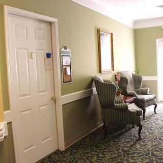 A hallway with two chairs and a door, featuring decorative wall art and patterned carpet.