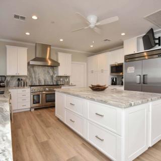A modern kitchen featuring white cabinets, marble countertops, stainless steel appliances, and an island with hardwood flooring.