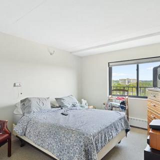 A bright bedroom with a bed, dresser, and window overlooking greenery.