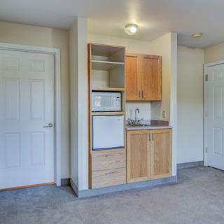 A compact kitchenette with wooden cabinets, a fridge, and a microwave in an apartment interior.